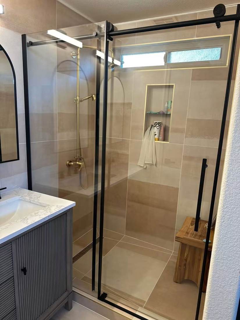 Walk-in shower with sliding glass door, brushed brass fixtures and linear drain