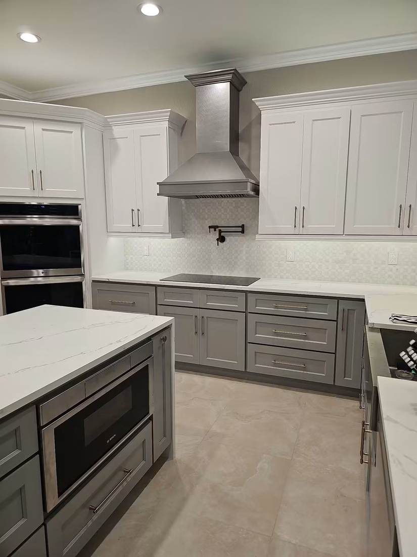 Remodeled kitchen with white and gray shaker cabinets, quartz countertops and stainless range hood