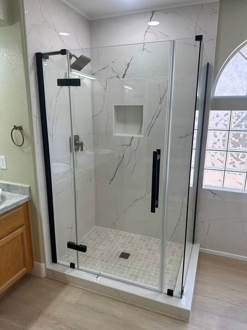 Frameless glass shower enclosure with white marble-look tile and black hardware