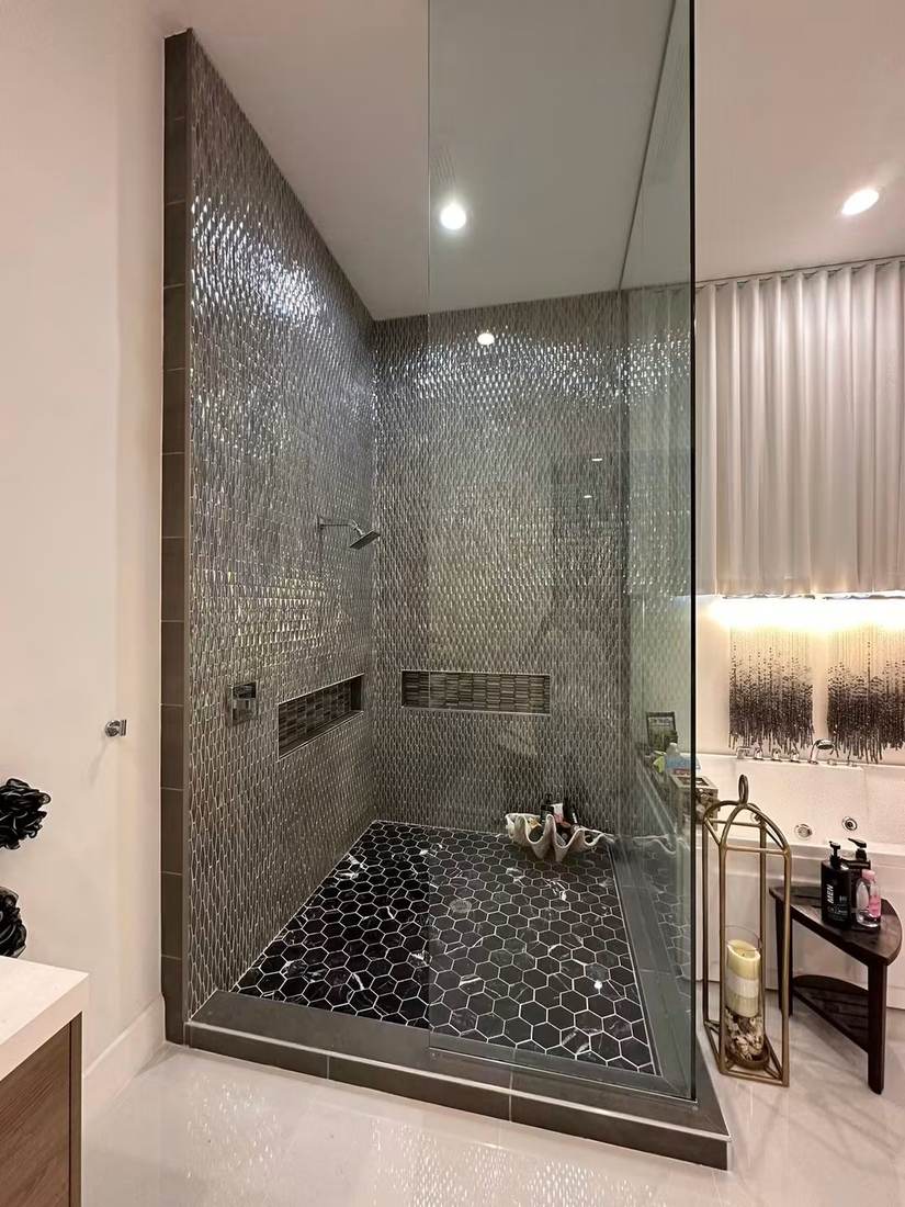 Glass-enclosed shower with metallic mosaic walls and black hexagon marble floor