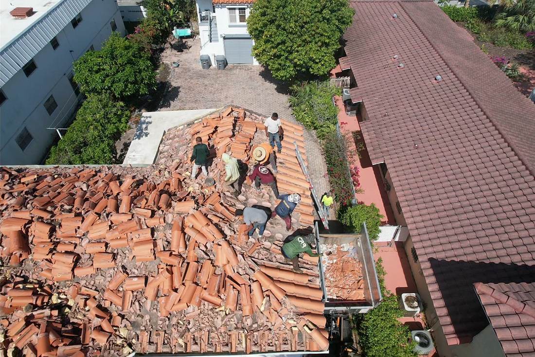 Crew removing old clay barrel tile from a roof into a dump trailer