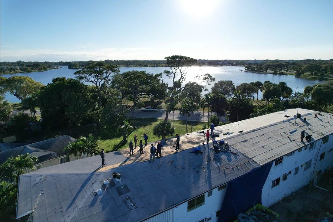 Drone view of a large roofing crew re-roofing a two-story apartment building by a lake