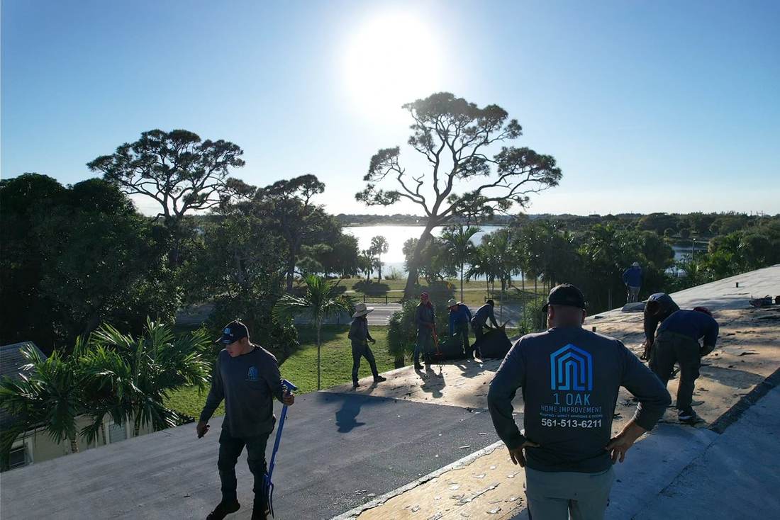 1 OAK Home Improvement roofing crew in company shirts tearing off a flat roof on a lakeside apartment building