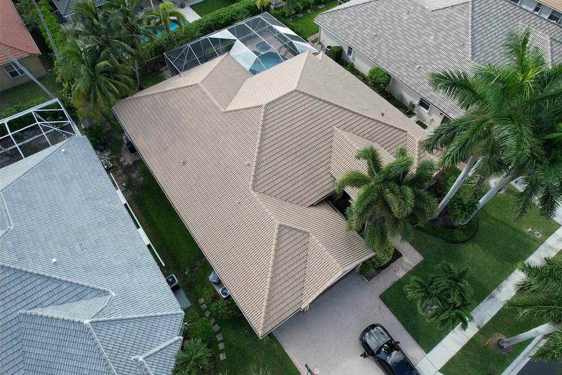 Aerial view of a home with a tan flat concrete tile roof, palm trees and screened pool