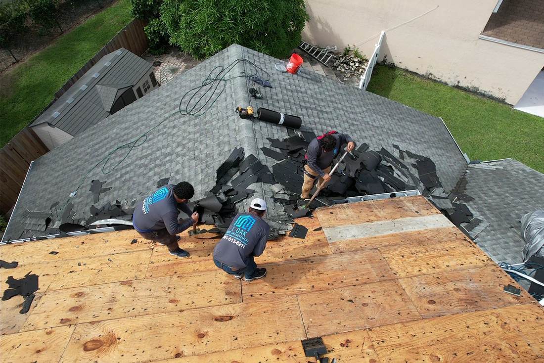 Three roofers in 1 OAK shirts tearing off old gray shingles